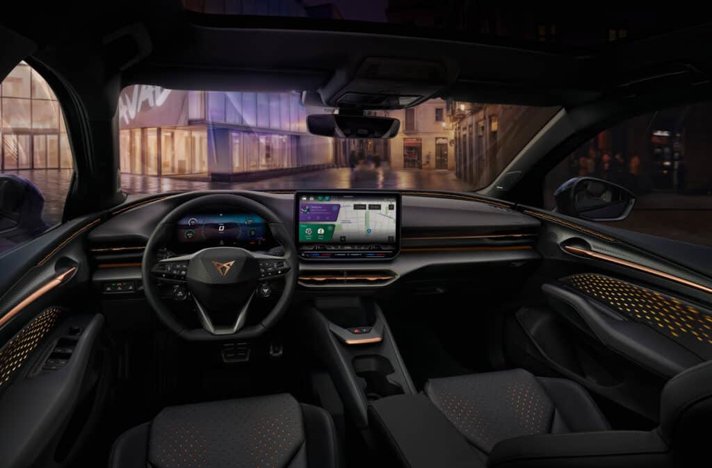 Auf diesem Bild ist der moderne und elegant gestaltete Innenraum eines Autos aus der Fahrerperspektive zu sehen, ausgestattet mit digitalen Displays, einem Multifunktionslenkrad und kupferfarbenen Akzenten, vor dem Hintergrund einer nächtlichen Stadtlandschaft.