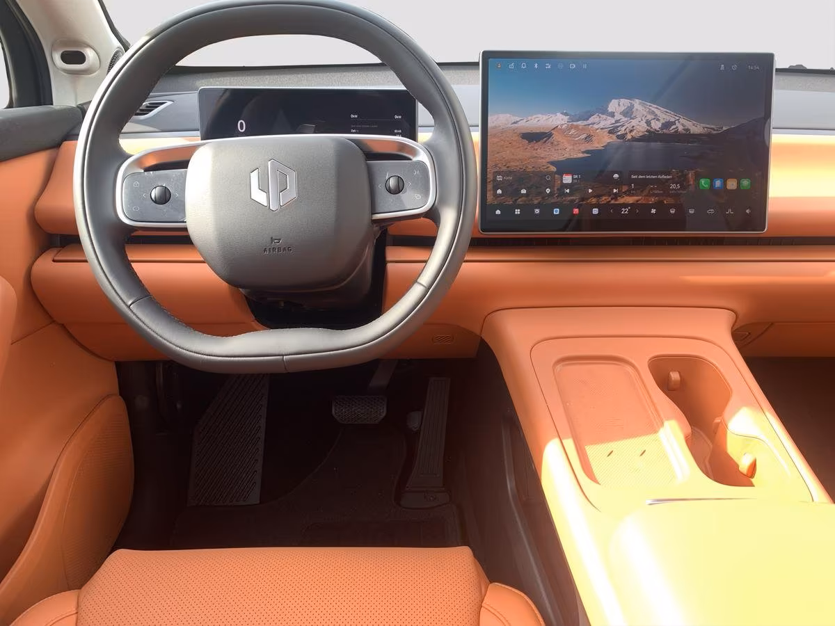 Auf diesem Bild ist der moderne und elegant gestaltete Innenraum eines Autos zu sehen, mit einem Lenkrad, einem digitalen Kombiinstrument und einem großen zentralen Infotainment-Bildschirm, alles in einer warmen orange-braunen Farbgebung.