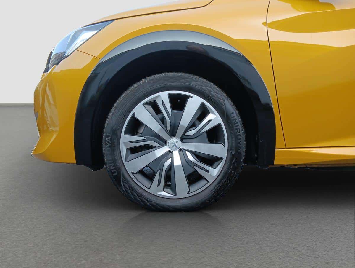 Auf diesem Bild ist der vordere linke Bereich eines gelben Autos mit einem schwarzen Radkasten und einem Rad mit Peugeot-Logo zu sehen.