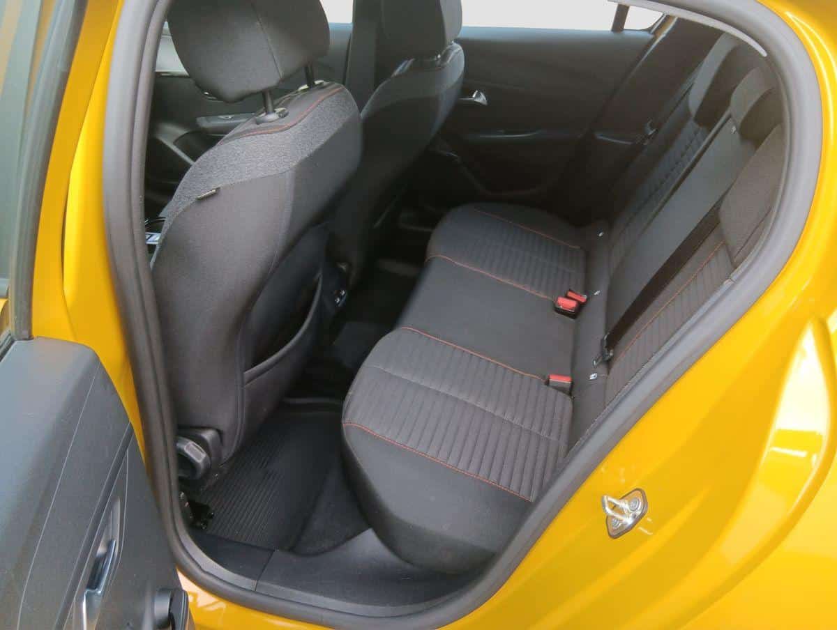 Auf diesem Bild ist der Innenraum eines gelben Autos zu sehen, genauer gesagt der Fond mit den schwarzen Rücksitzen und einer geöffneten hinteren Tür.