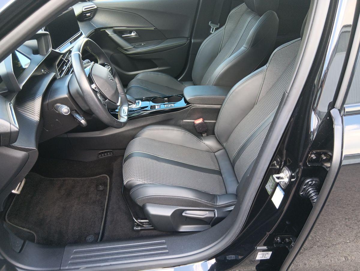 Auf diesem Bild ist der moderne, schwarz gestaltete Innenraum eines Autos von der Fahrerseite aus zu sehen, inklusive Lenkrad, Vordersitzen und Armaturenbrett.