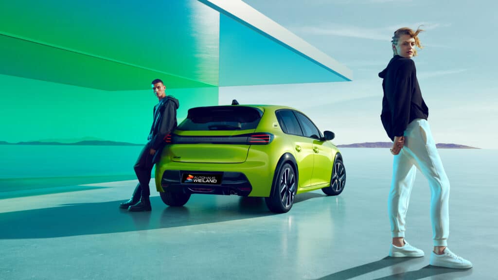 Gebrauchtwagen 5 Auf diesem Bild ist ein leuchtend grüner Peugeot 208 zu sehen, flankiert von einem sich anlehnenden Mann und einer stehenden Frau, alles in einer stilisierten Umgebung mit architektonischen Elementen in Grün- und Blautönen sowie einer weitläufigen Landschaft mit Wasser und Bergen im Hintergrund.