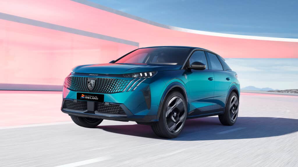 Gebrauchtwagen 2 Auf diesem Bild ist ein türkisfarbener Peugeot 3008 SUV zu sehen, der auf einer Straße vor einer Kombination aus moderner, rosafarbener Architektur und einer weiten Landschaft fährt.