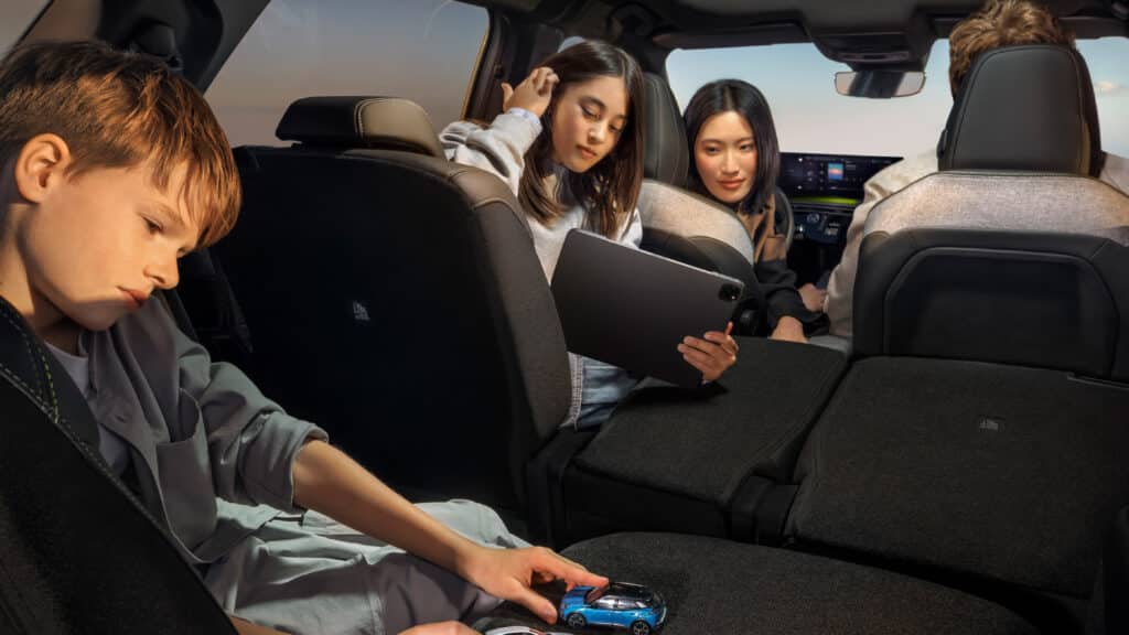 Gebrauchtwagen 4 Das Bild zeigt den Innenraum eines Autos, in dem ein Junge auf dem Rücksitz mit einem Spielzeugauto spielt, während zwei junge Frauen daneben ein Tablet benutzen und im Hintergrund eine weitere Person fährt.