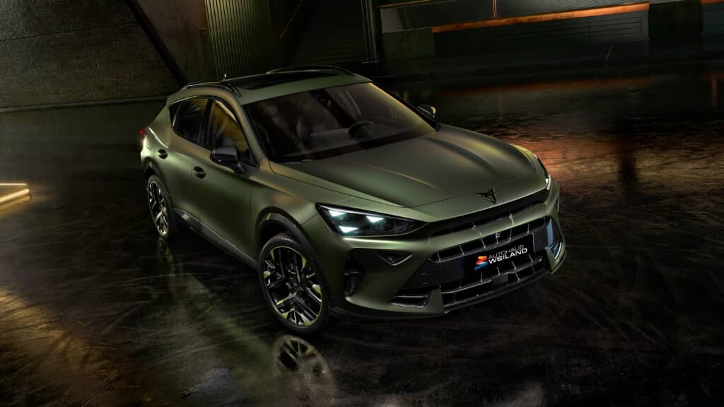 Gebrauchtwagen 1 Auf diesem Bild ist ein mattgrünes Crossover-Fahrzeug der Marke Cupra in einer dunklen, industriell anmutenden Umgebung mit reflektierendem Boden zu sehen.